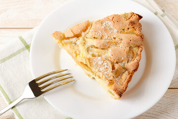 Close-up of large piece of sweet and sour apple pie and fork on a white plate over a white wood table. Easy recipe for sweet homemade baking. Breakfast pastries.