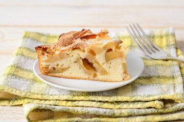 Large piece of sweet and sour apple pie on a white plate over yellow-green checkered table napkin. Easy recipe for sweet homemade baking. Breakfast pastries.