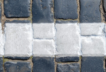 Fragment of a cobblestone pavement with a white strip of road markings, painted with special paint. Horizontal orientation, selective focus.