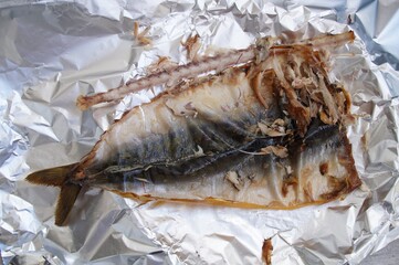 Remains of smoked mackerel lying on a crumpled silver aluminium foil. 