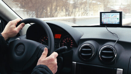 Close-up shot of a man driving a car in winter city. GPS device on the dashboard helps him to find...