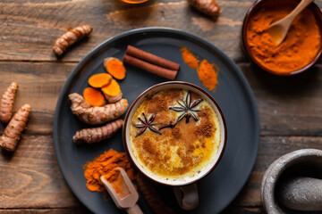 Golden milk in white mug, turmeric latte made with curcuma and other spices: cinnamon, anise. Healthy hot winter drink, natural, organic beverage. Close up, front view. Dark wooden rustic background