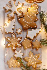 Delicious homemade gingerbread cookies with white icing. Christmas lights, branch of fir tree, dry orange slices. White wooden background, flat lay, top view. Festive holiday atmosphere, family time