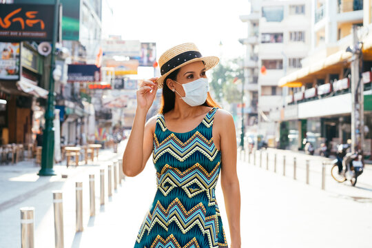 Young brunette woman traveling in Bangkok, Thailand in popular Khao San Road during pandemic Coronavirus. 20s Hispanic in a protective mask wear summer sleeveless summ dress in Asia. With Copy space