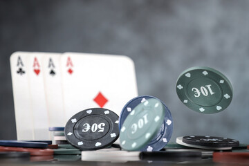 A pair of aces, hearts and diamonds, on a deck of playing cards. Poker playing chips on a dark and light blue background. Online gambling. Addiction. Falling playing cards and poker chips