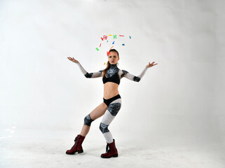 beautiful girl in a robot suit throws up multi-colored letters and does gymnastic exercises on a white background