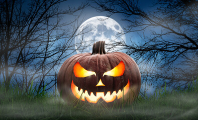 One spooky halloween pumpkin, Jack O Lantern, with an evil face and eyes on the grass with a misty...