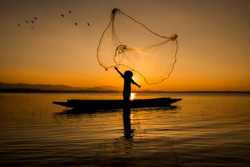 Silhouette fisherman throwing net casting fish in early morning with wooden boat with a flock of...