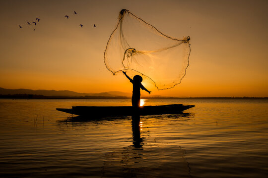 Silhouette fisherman throwing net casting fish in early morning with wooden boat with a flock of birds, Fisherman life style