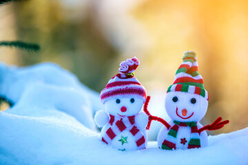 Two small funny toys baby snowman in knitted hats and scarves in deep snow outdoors on bright blue and white copy space background. Happy New Year and Merry Christmas greeting card.