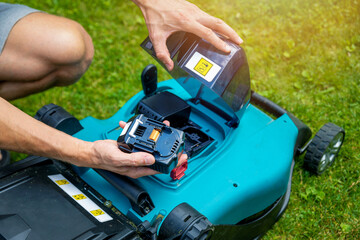 man putting battery into electric cordless lawn mower - obrazy, fototapety, plakaty