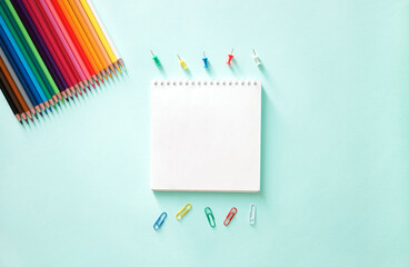 flat lay composition with Clear sheet note book, paper clips, stationery buttons and colour pencils on a blue background.  . Back to school, college, education concept. Space for text, copy space. 