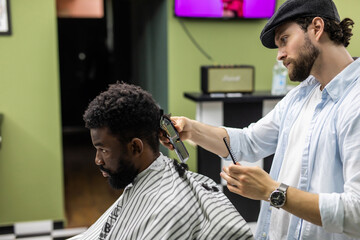 Side view of serious man with stylish modern haircut looking forward in barber shop. Hand of barber keeping razor and cutting hair on head of client. Concept of shaving.