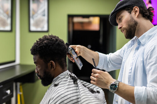 Closeup of process of trimming of hair in barber shop. Qualified barber keeping clipper in hands and correcting shape of hair to male client sitting on chair. Concept of haircut and shaving.