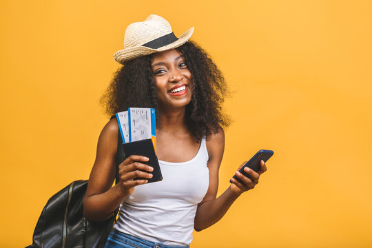 Travel, tourism and vacation concept - happy young african american black woman with air tickets using phone isolated over yellow background.