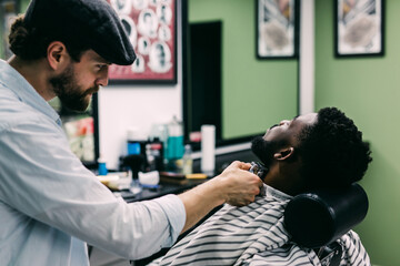 A barber is going through the electric cutting and shaving machine for the beard of an African-American boy.