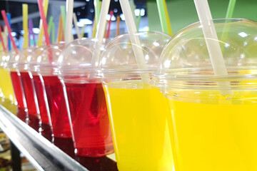 Colorful refreshment drinks lemonade in plastic glasses, in stand with takeaway food.