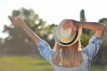 Happy blonde woman with hand raised in the air and with another hand holding a white hat. Blonde...