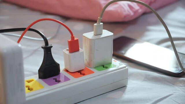 Hand holding mobile phone charging battery connected plugs on the bed.