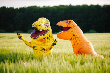 Two yellow and orange dinosaur dino tyrannosaurus running biting each other and having fun in green...