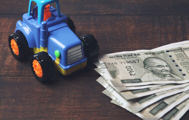 Obraz premium Plastic toy tractor with Indian currency on wooden table - Vehicle loan concept 