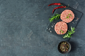 Raw burger cutlets made from minced fresh meat with rosematy and chili on a slate board top view.