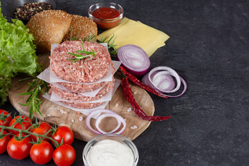 Fresh raw ingredients for homemade burger on black background