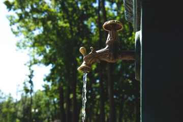Open beautiful vintage water tap in a park in in hot summer. A faucet with a pouring water. Economical use of water. Side view