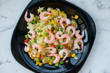 Rice with vegetables and shrimp on a black plate, standing on the table