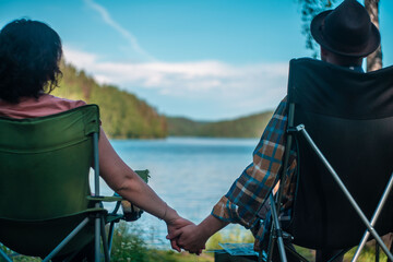 young couple holding hands sitting by the lake. family camping. romantic evening on the lake