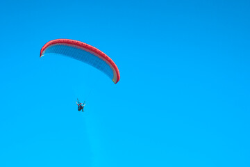 Doubles paragliding against a clear blue sky. A multi-colored papaplan flies in the clear sky closeup.