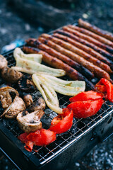 Many long sausages with mushrooms, tomatoes and grilled bell pepper. Cooking vegetables on charcoal. Food in nature. Picnic..