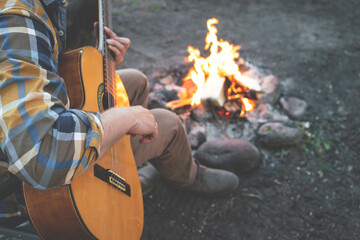 camping in the woods. man plays the guitar by the fire in nature. summer camping. relaxation in...
