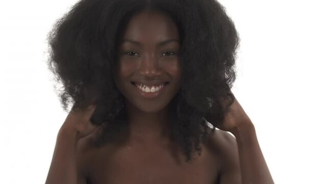 Portrait of young black woman laughing on white background and playing with hair