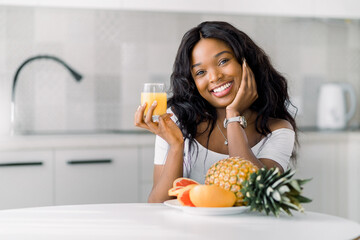 Portrait of young smiling african woman sitting indoors at the cozy home kitchen interior, at the...