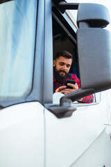 Young handsome bearded man driving his truck and using smart phone.