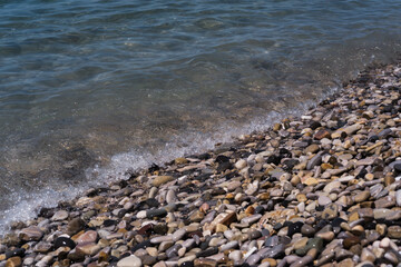 A wave rolls over the rocky shore. Pebble beach. Seashore.