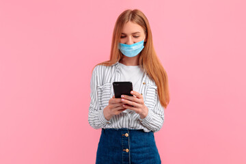 Young beautiful woman in a medical protective mask on her face using a mobile phone on an isolated pink background