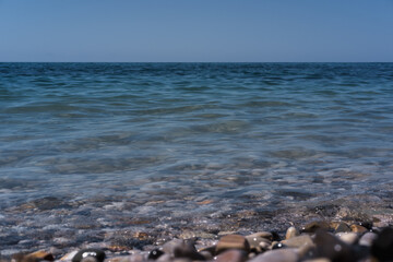 A wave rolls over the rocky shore. Pebble beach. Seashore.