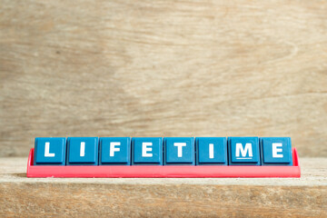 Tile letter on red rack in word lifetime on wood background