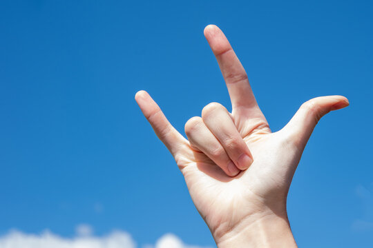 love gesture, finger sign i love you against the blue sky, concept sign language, non-verbal communication