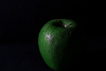 one green apple wet with water drops on black background