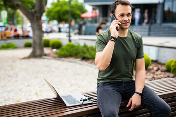 Fototapeta premium Handsome smiling young man sitting on a bench and talking on mobile phone