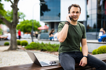 Handsome smiling young man sitting on a bench and talking on mobile phone