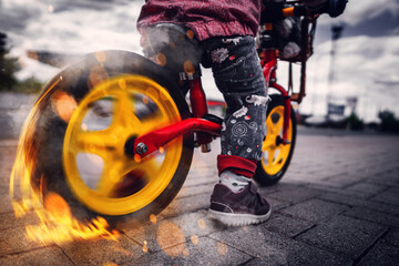 Kind auf einem Laufrad macht einen Burnout auf der Straße mit Feuer und Rauch