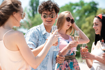Obraz premium Cheers, clinking glasses. Seasonal feast at beach resort. Group of friends celebrating, resting, having fun in sunny summer day. Look happy and cheerful. Festive time, wellness, holiday, party.