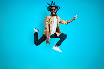 Fototapeta na wymiar Full length of cheerful young African man in casual wear shouting and gesturing while hovering against blue background