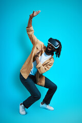Full length of playful young African man wearing virtual reality glasses while standing against...