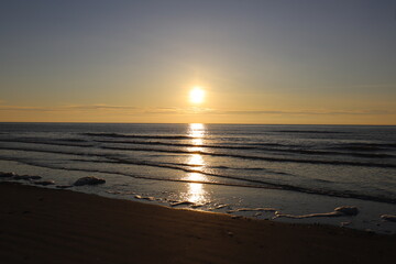 Beautiful warm golden sunlit clouds during sunset perfectly reflecting in the sand on a beach.