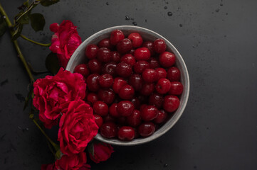 cherries in a bowl on the blak background with red rose